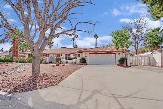 single story home featuring an attached garage, a tiled roof, concrete driveway, a gate, and stucco siding