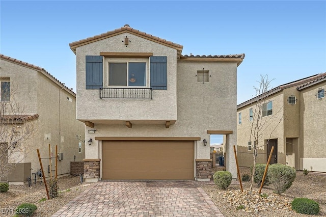 mediterranean / spanish house featuring a garage, stone siding, decorative driveway, and stucco siding