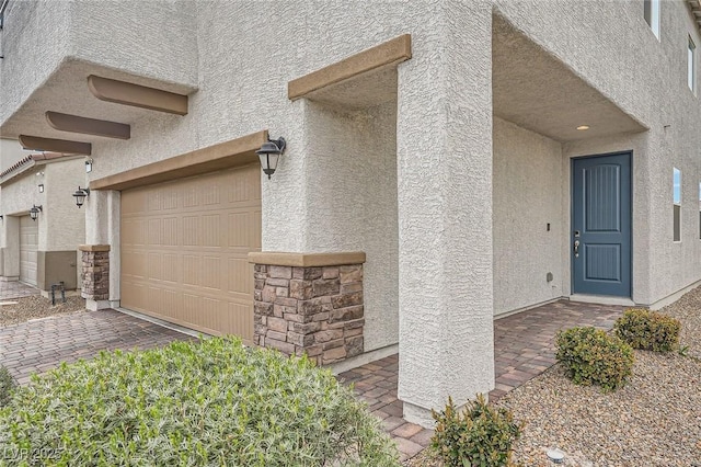 view of exterior entry with a garage, stone siding, and stucco siding