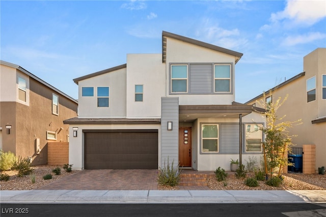 modern home with decorative driveway, fence, an attached garage, and stucco siding