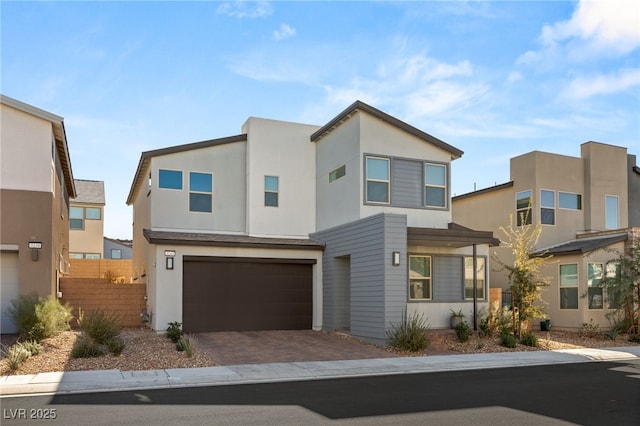 modern home featuring decorative driveway, fence, an attached garage, and stucco siding