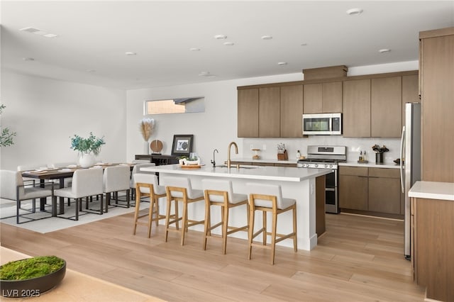 kitchen with light wood finished floors, a center island with sink, appliances with stainless steel finishes, a kitchen breakfast bar, and a sink