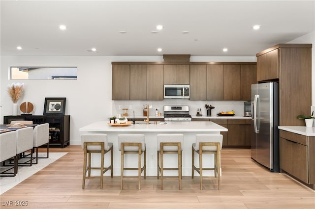 kitchen with light wood finished floors, appliances with stainless steel finishes, and a kitchen breakfast bar