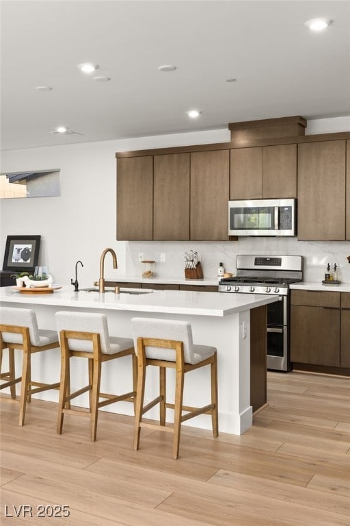 kitchen featuring a breakfast bar area, stainless steel appliances, tasteful backsplash, light countertops, and a sink