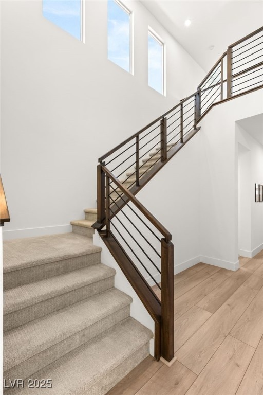 stairway with recessed lighting, a towering ceiling, baseboards, and wood finished floors