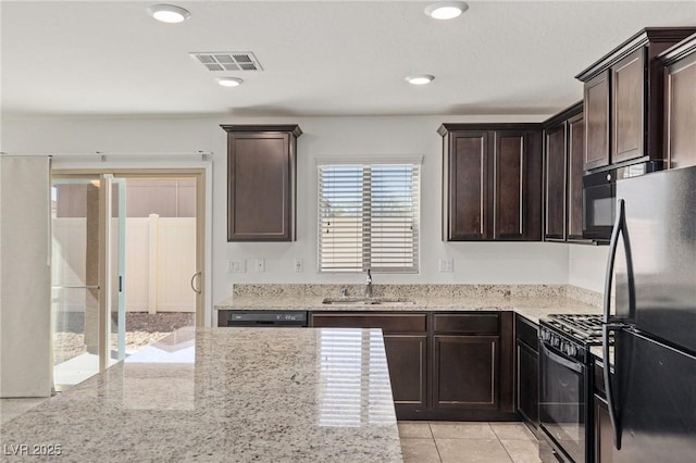 kitchen with light stone counters, visible vents, a sink, dark brown cabinets, and black appliances