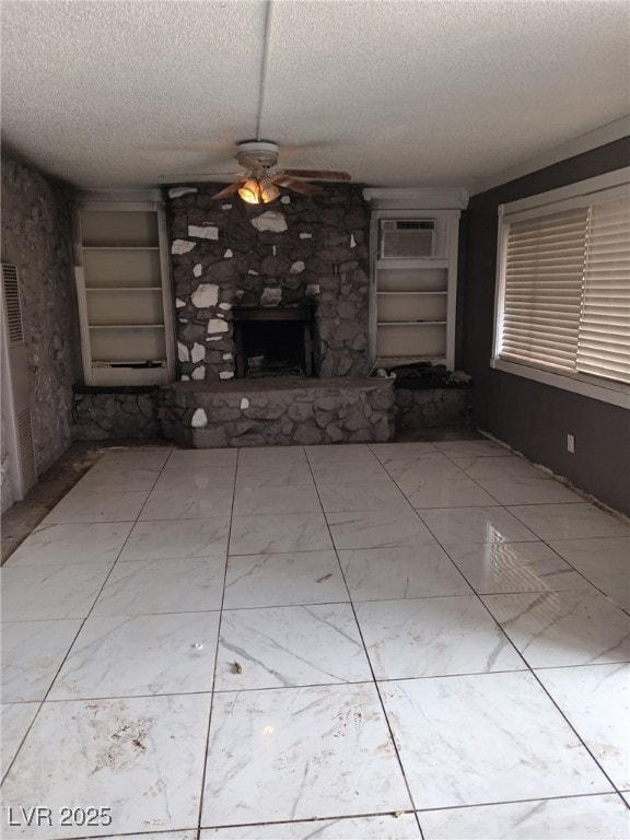 unfurnished living room featuring a large fireplace, a textured ceiling, a ceiling fan, and a wall mounted AC