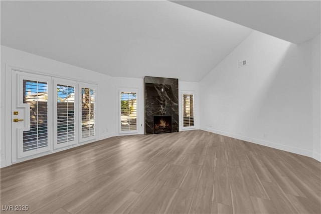 unfurnished living room with lofted ceiling, a premium fireplace, wood finished floors, and visible vents