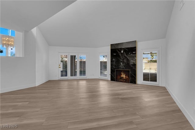 unfurnished living room with a notable chandelier, light wood-style flooring, baseboards, and a premium fireplace