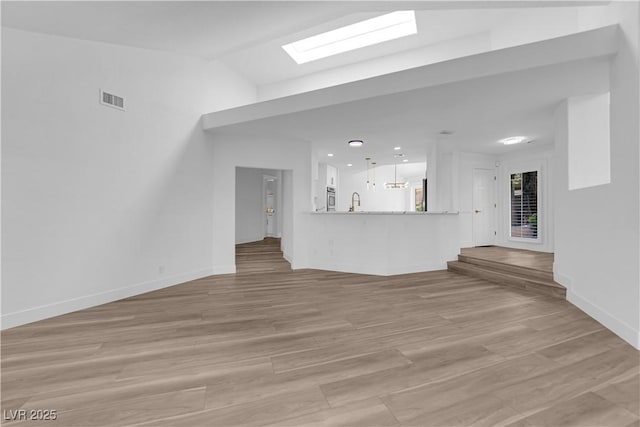 unfurnished living room featuring a sink, visible vents, baseboards, light wood-style floors, and lofted ceiling with skylight