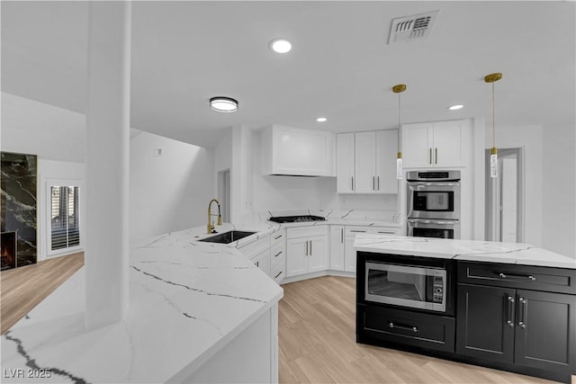 kitchen with visible vents, appliances with stainless steel finishes, white cabinetry, a sink, and dark cabinetry