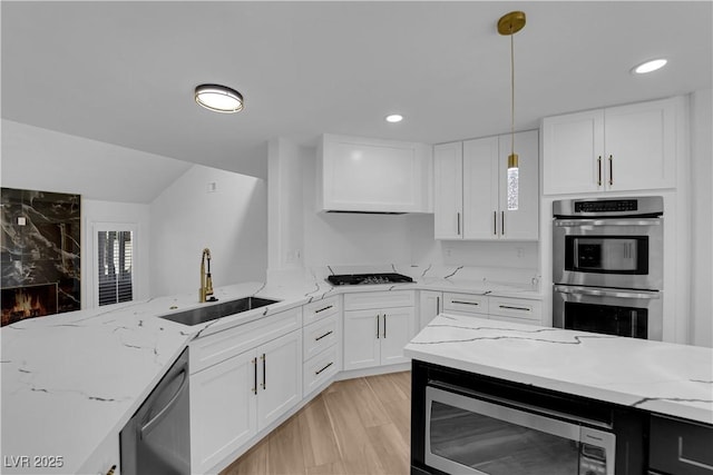 kitchen with light stone counters, appliances with stainless steel finishes, white cabinets, and a sink