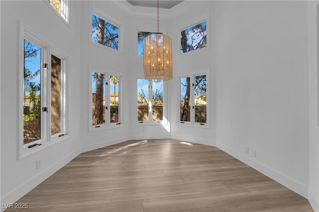 unfurnished dining area featuring baseboards, wood finished floors, a towering ceiling, and a notable chandelier