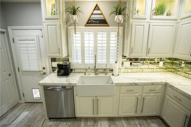 kitchen with backsplash, wood finish floors, stainless steel dishwasher, white cabinetry, and a sink