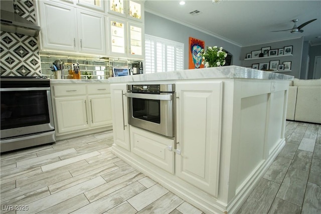 kitchen featuring wood finish floors, ornamental molding, stainless steel appliances, open floor plan, and backsplash