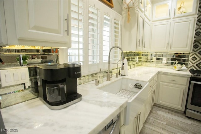 kitchen with a sink, white cabinetry, gas stove, decorative backsplash, and light stone countertops