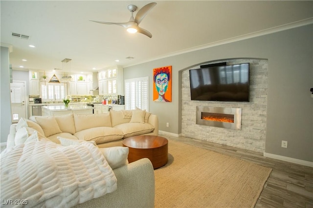 living area with a wealth of natural light, visible vents, a glass covered fireplace, and wood finished floors