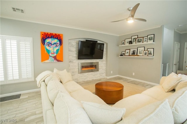 living room with visible vents, crown molding, wood finished floors, a glass covered fireplace, and a ceiling fan