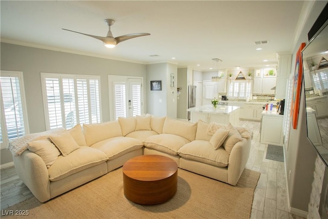 living room featuring light wood-type flooring, visible vents, a ceiling fan, and crown molding