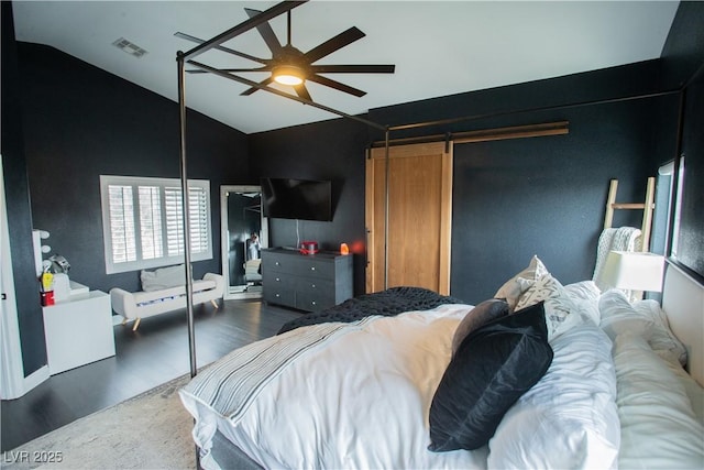 bedroom with wood finished floors, visible vents, lofted ceiling, ceiling fan, and a barn door