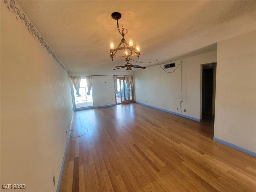 spare room featuring visible vents, baseboards, ceiling fan with notable chandelier, wood finished floors, and a textured ceiling