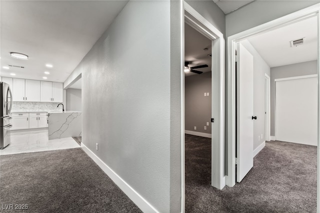 hall featuring visible vents, dark carpet, and baseboards