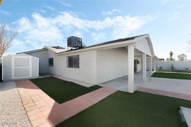 rear view of property with an outbuilding, a patio, a storage shed, central AC, and stucco siding