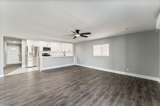 unfurnished living room featuring a sink, a ceiling fan, baseboards, and dark wood-style flooring