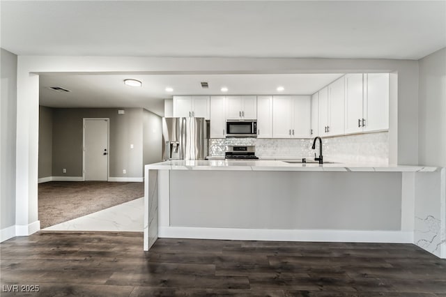 kitchen featuring appliances with stainless steel finishes, a peninsula, light countertops, white cabinetry, and a sink