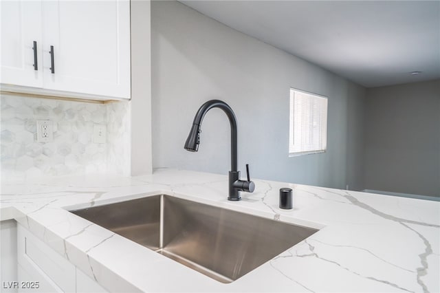 interior details featuring tasteful backsplash, white cabinets, a sink, and light stone countertops