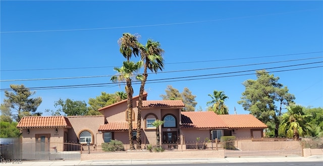 mediterranean / spanish home with a fenced front yard, a tile roof, and stucco siding