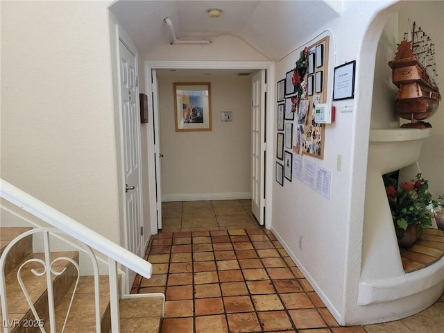 corridor with vaulted ceiling, light tile patterned flooring, stairs, and baseboards