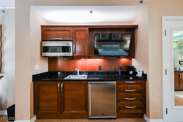 bar with built in refrigerator, a sink, baseboards, stainless steel microwave, and indoor wet bar