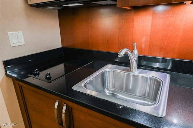 kitchen with black electric stovetop, a sink, ventilation hood, brown cabinets, and dark countertops