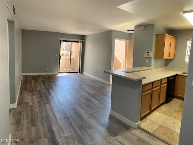 kitchen with baseboards, dishwasher, open floor plan, a peninsula, and light countertops