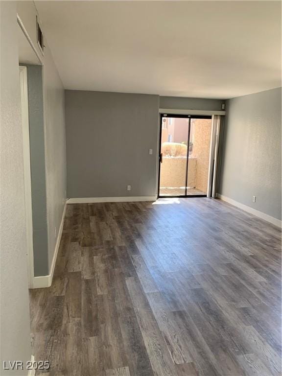 empty room with dark wood-type flooring, visible vents, and baseboards