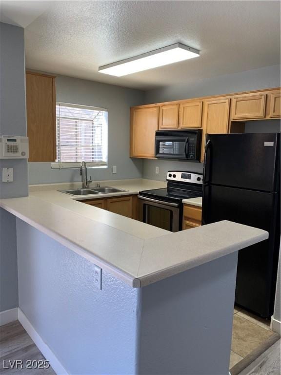 kitchen featuring a peninsula, light countertops, a textured ceiling, black appliances, and a sink