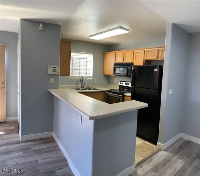 kitchen featuring a peninsula, light countertops, light brown cabinetry, black appliances, and a sink