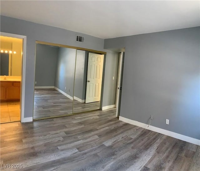 unfurnished bedroom featuring baseboards, visible vents, a closet, and wood finished floors