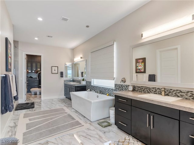 bathroom with a freestanding tub, two vanities, recessed lighting, a sink, and marble finish floor