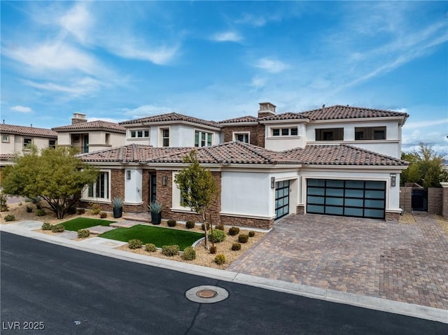 view of front facade with a tiled roof, stucco siding, an attached garage, and decorative driveway