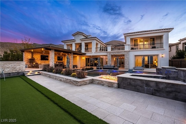 back of house at dusk with a balcony, a patio area, and stucco siding