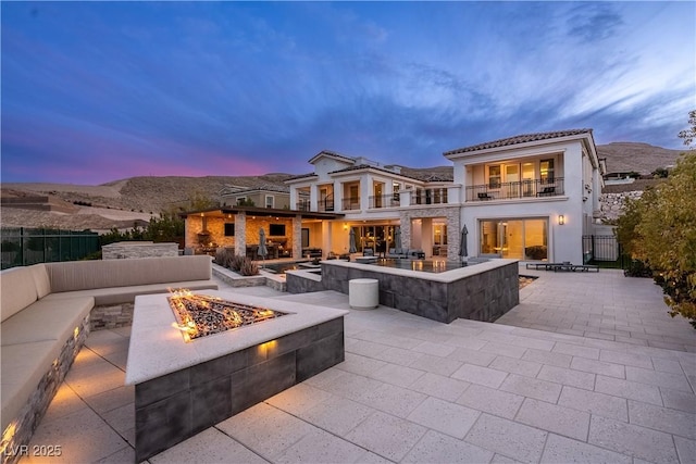 rear view of house featuring fence, an outdoor fire pit, stucco siding, a balcony, and a patio area