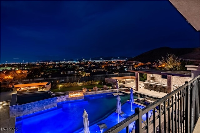 pool at night featuring outdoor dry bar, a fenced in pool, exterior kitchen, and a fenced backyard