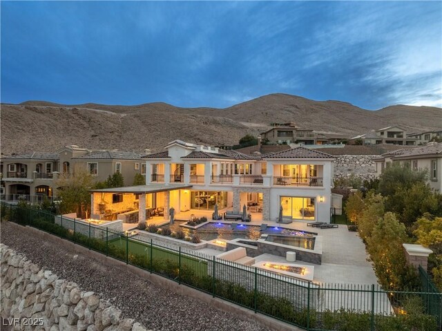 back of house with a fenced front yard, a balcony, a patio area, a mountain view, and an in ground hot tub