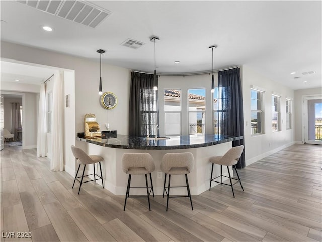 kitchen with light wood finished floors, visible vents, a breakfast bar, and a sink