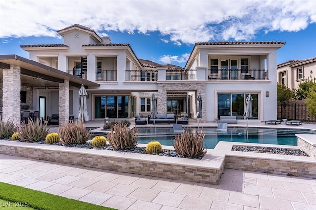 back of property with fence, stucco siding, an outdoor hangout area, a balcony, and a patio area