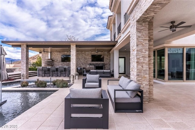 view of patio / terrace with outdoor dry bar, an outdoor living space with a fireplace, an outdoor kitchen, and a ceiling fan