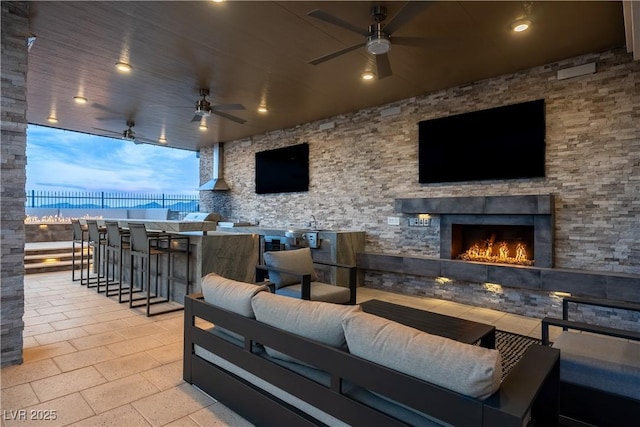 view of patio with fence, an outdoor living space with a fireplace, outdoor wet bar, a ceiling fan, and a sink