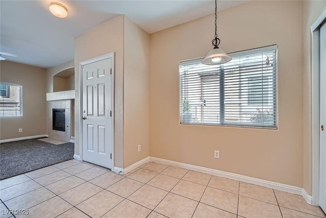 unfurnished dining area with baseboards, a tiled fireplace, and light tile patterned floors